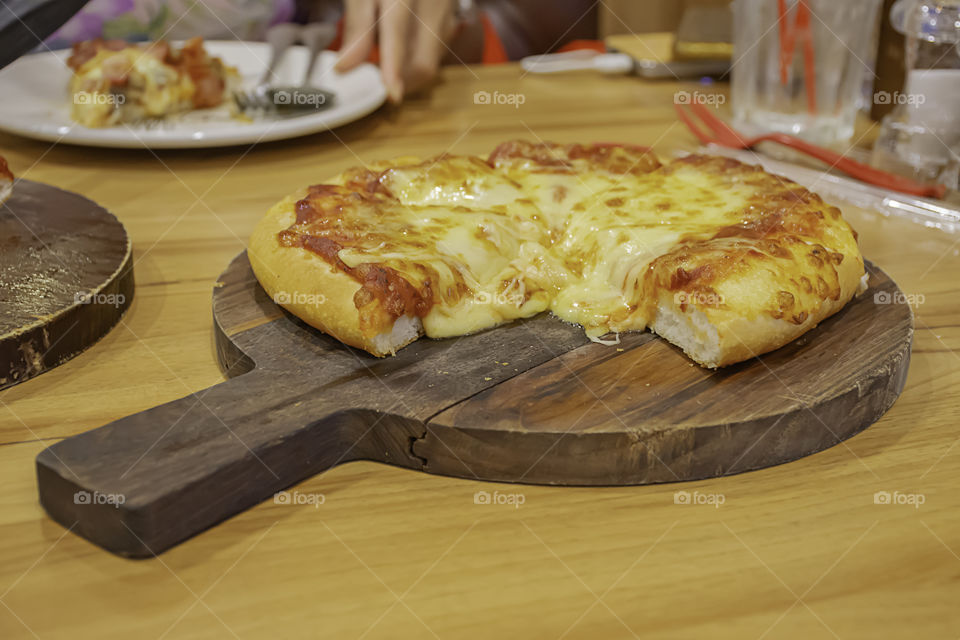 Pizza with ham and cheese on the wooden tray is placed on the table.