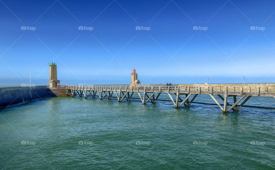 Port and starboard signal lighthouses and piers of the port entry of fécamps harbor on the Normandy coast in France under a deep clear blue sky in springtime.