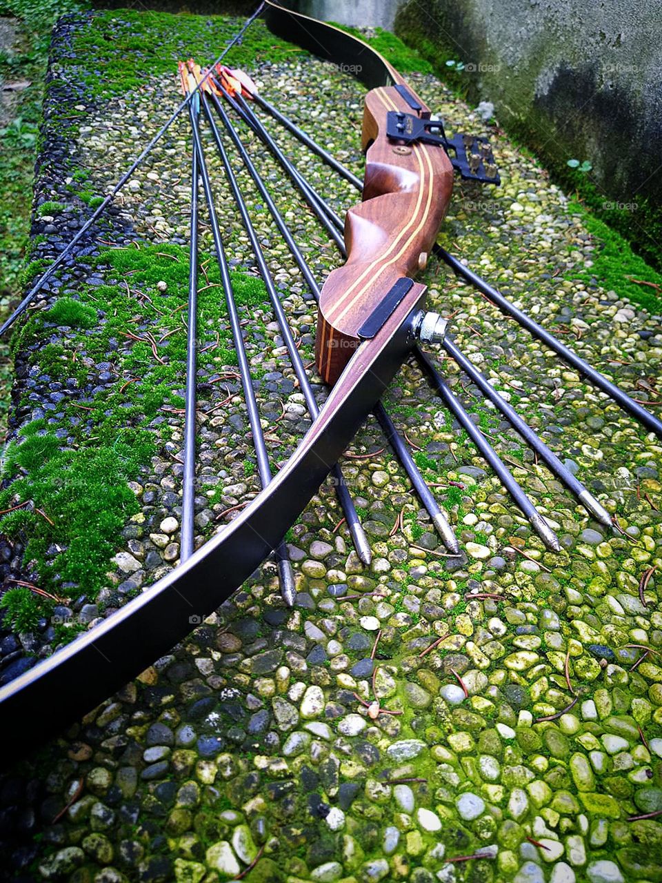 Metal and wood.  Arrows with metal tips and a professional wooden crossbow lie on a stone slab covered with green moss.