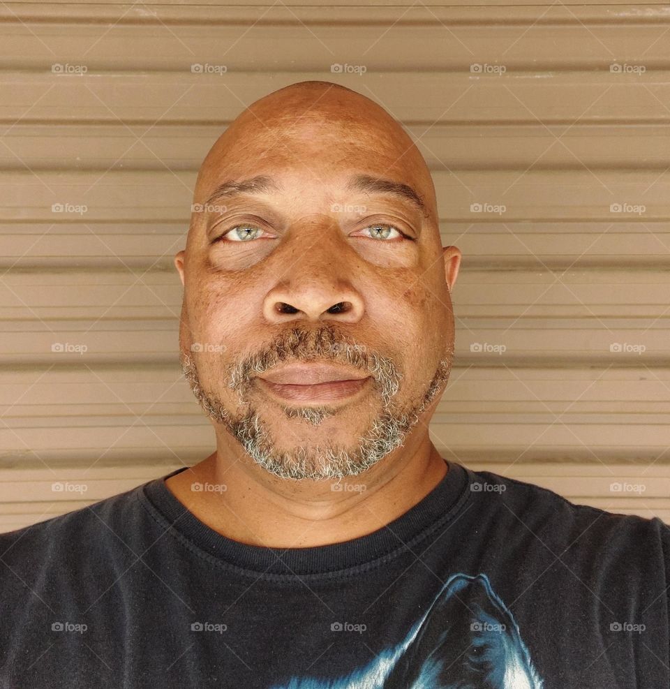 Self portrait of a man with a bold head and a gray beard looking at the camera