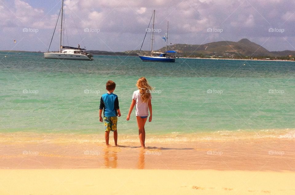 Siblings walking on the beach in Sint Maarten, sailboats and mountains in background 