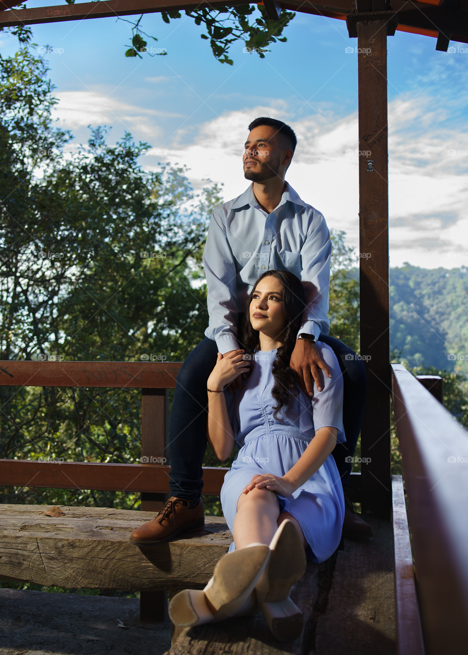 Couples of young people sitting in a viewpoint of a mountain while looking to the horizon, in a sunny day.