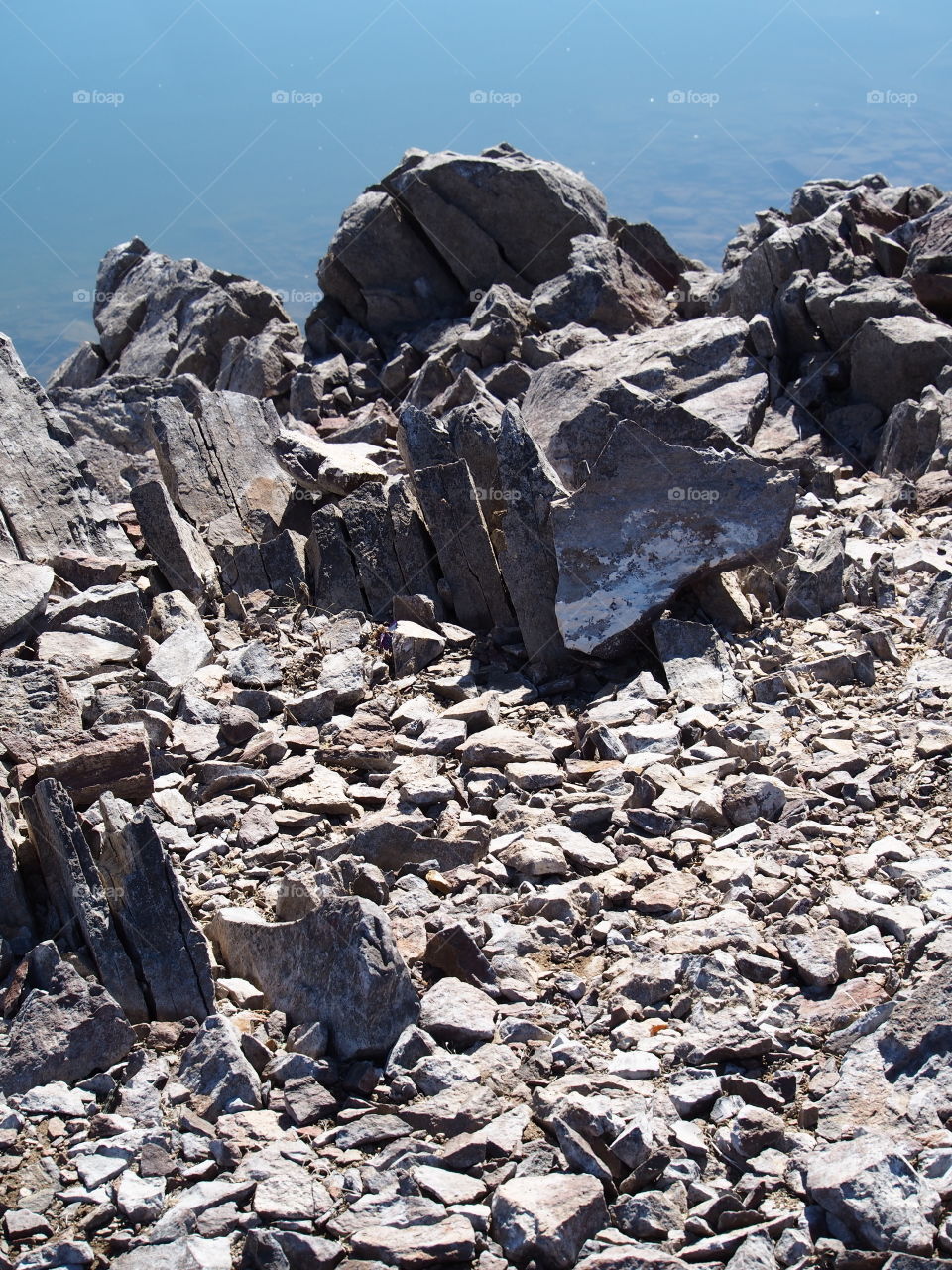 Jagged rocks and boulders along the shoreline of Ochoco Lake in Central Oregon on a sunny spring day.