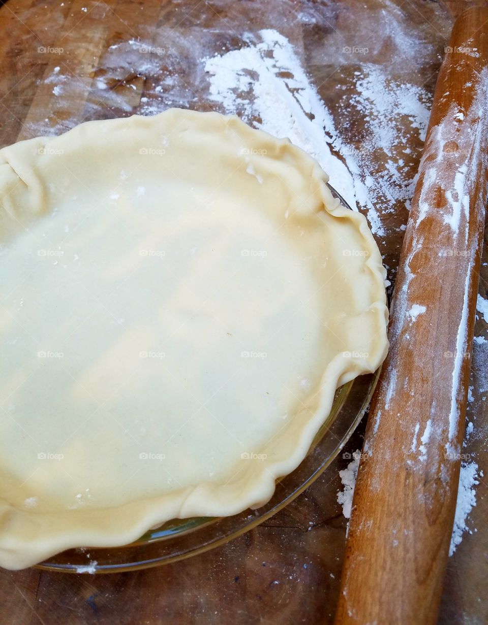 Pie crust in bottom of glass pie dish, old wooden rolling pin used