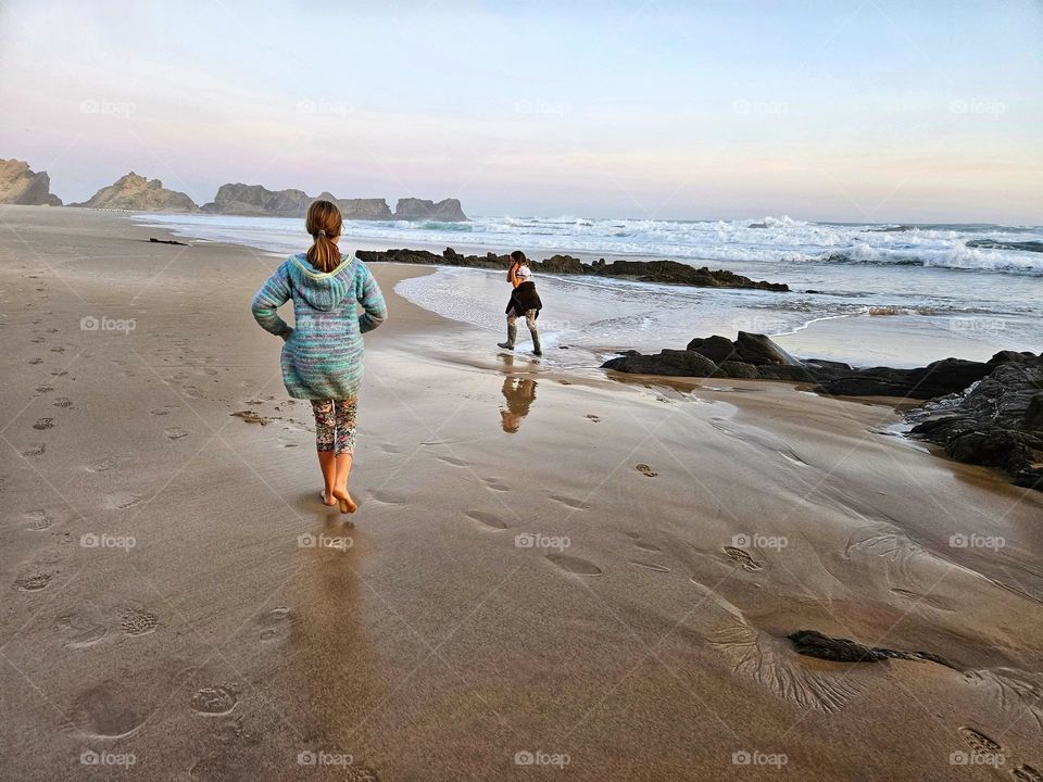 sisters running along a beach while it low tide, and early morning with rocks in the distance