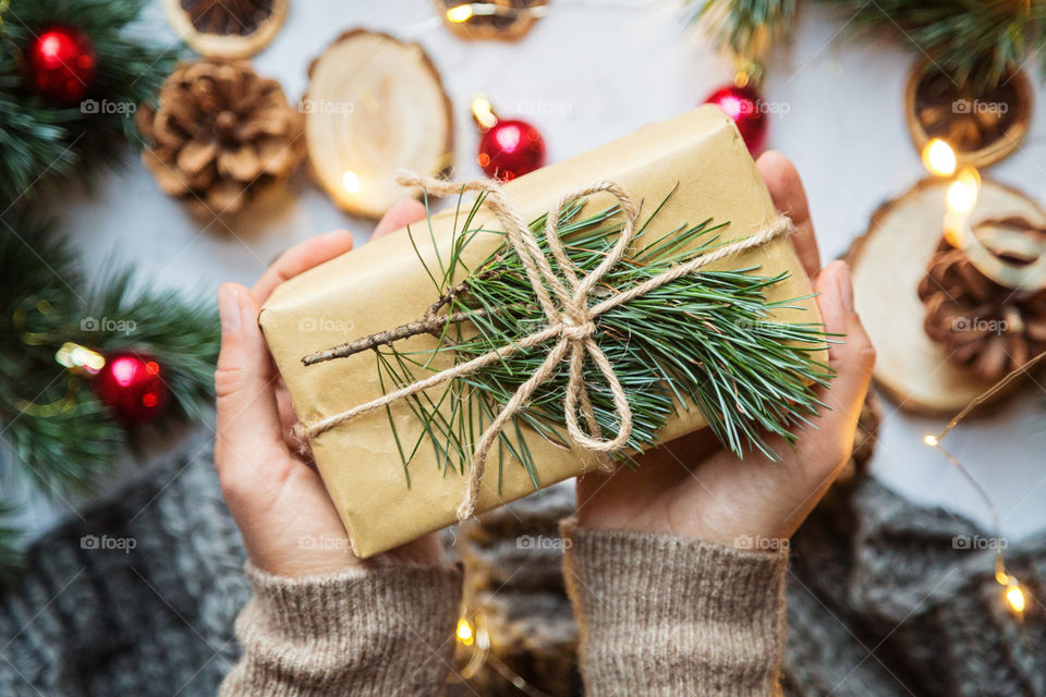 Hands holding packed Christmas gift in craft box with tree