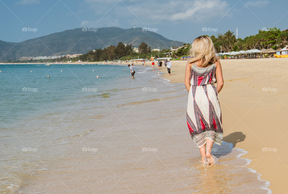 Beautiful blond hair girl is walking on a sea beach