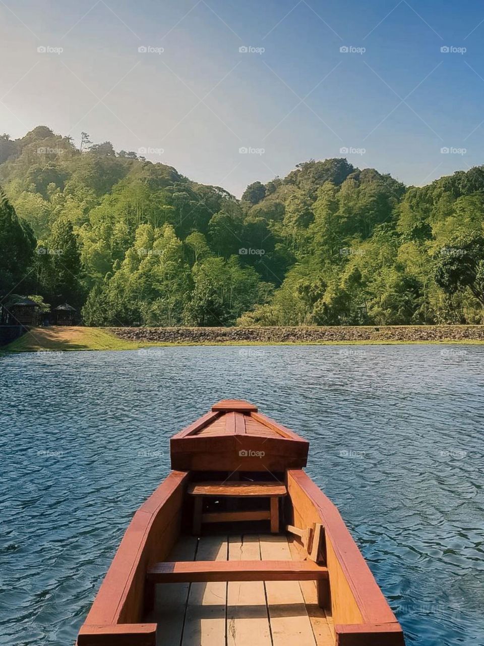 Close-up view of the front of a wooden boat floating on water with a backdrop of green mountains and bright blue sky