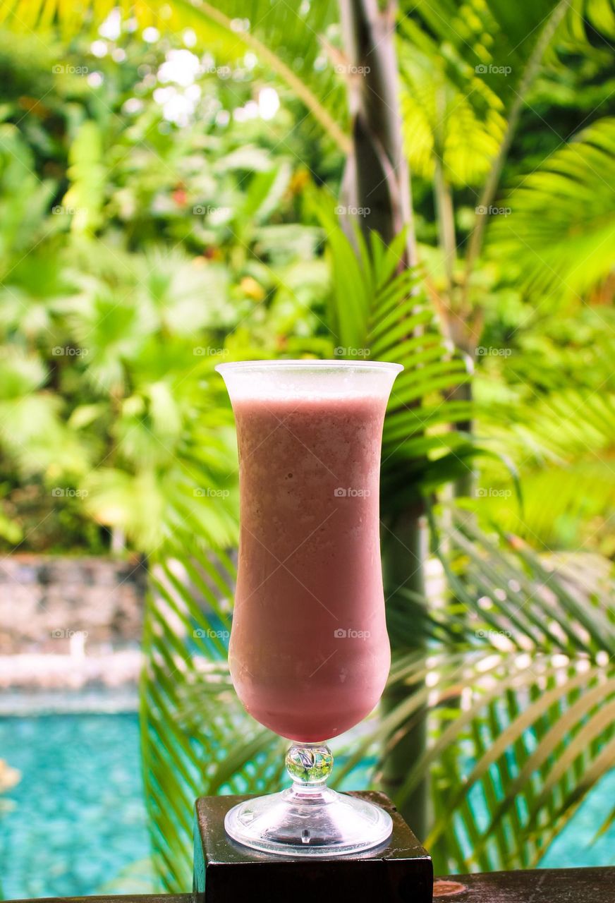 Smoothie with exotic fruits,  blurred background with palm trees next to the pool