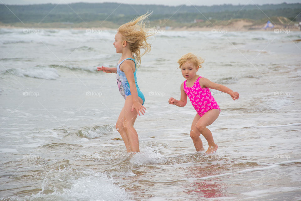 Twi sisters playing at the beach of Tylösand outside Halmstad in Sweden. It's about to get stormy weather but the girls is having fun swimming and playing in the water.