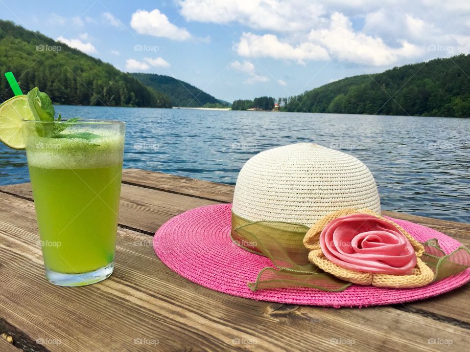 Mint lemonade glass and summer pink hat near the lake