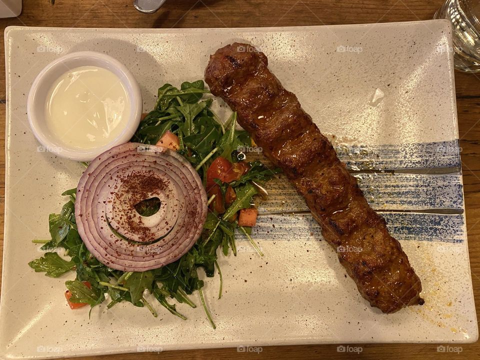 Lamb shish kebab with vegetable or salad on the side with slice of onion on the top.