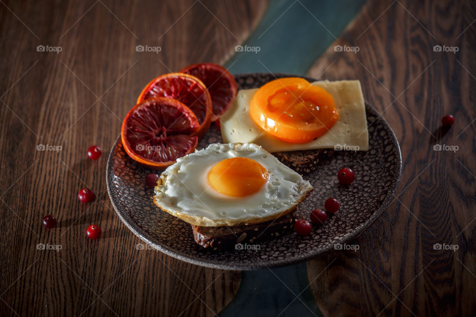 Grain bread with egg, tomato, cheese and bacon on ceramic plate with red orange to desert