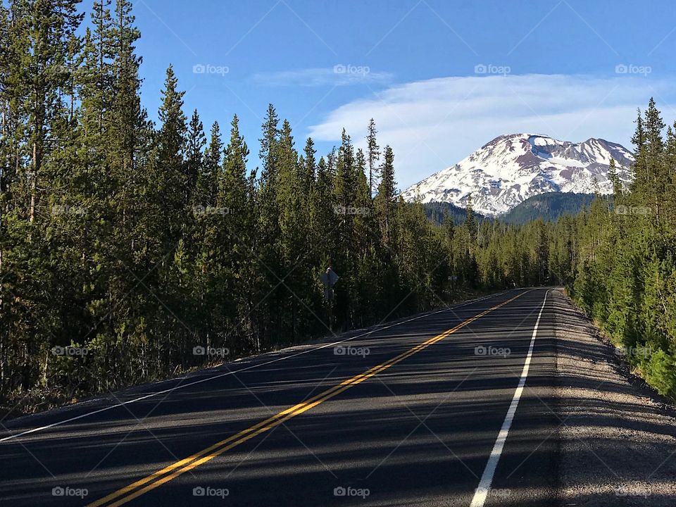 The Cascades Lakes Highway in the forests of Central Oregon with the snow covered South Sister in the background on a sunny fall day. 