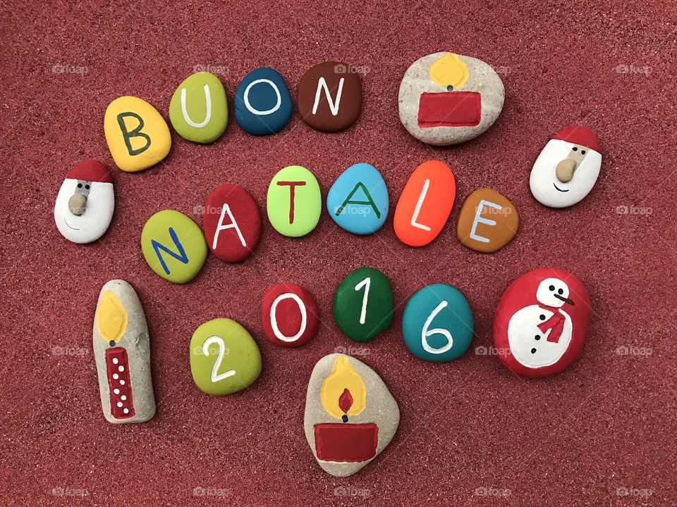 Buon Natale, italian Merry Christmas on colored stones over red sand 