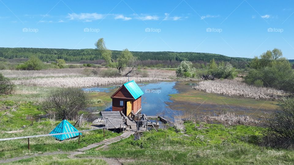 A spring with a font and a chapel with a blue roof on the lake with reeds and bushes