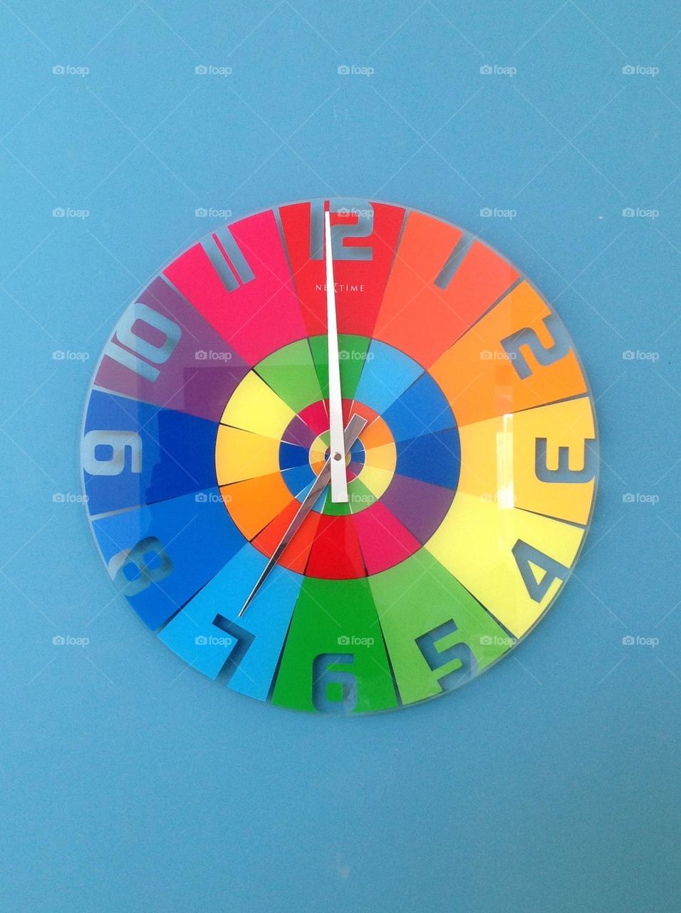 A beautiful and colorful clock hanging on a blue wall with circles within circles 