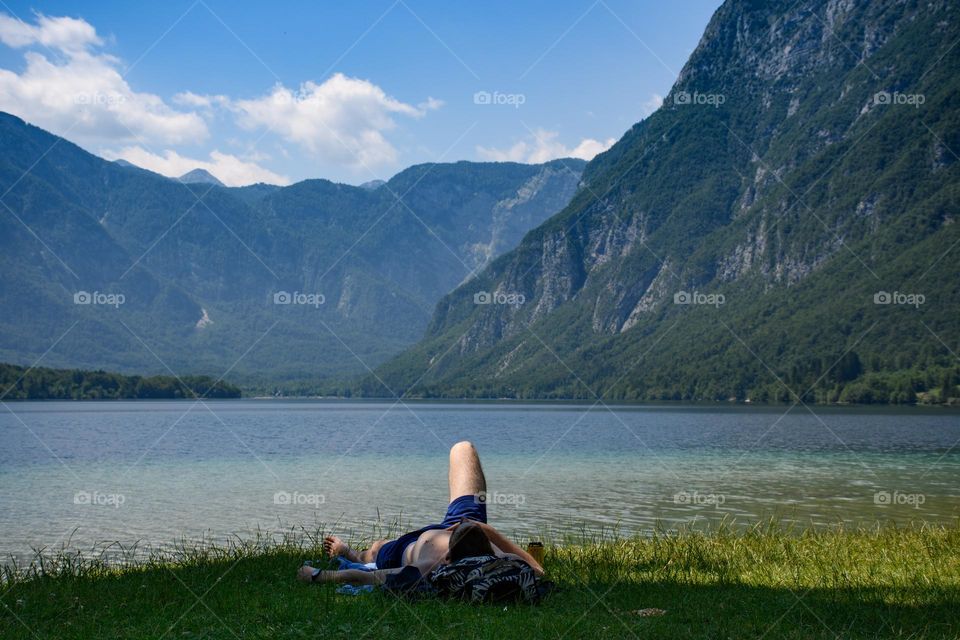 Man laying and relaxing on shore of amazing lake in the mountains in the summer