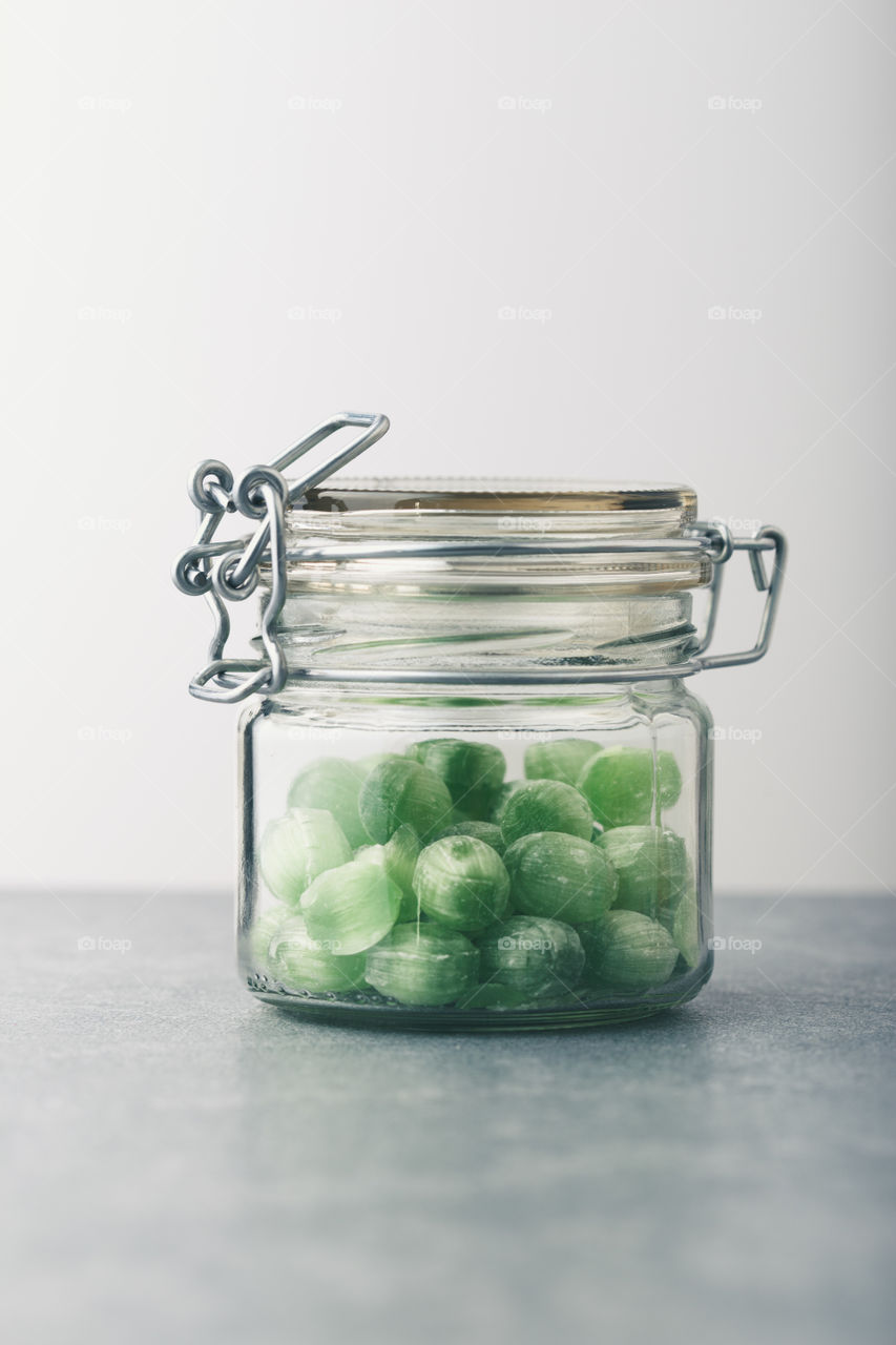 Jar filled with green mint candies on table. Plain background