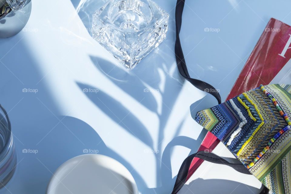 Items and image are selected and prepared for travel.  A blue shirt, a glass of clean water and sunglasses, reading magazines on a blue background.