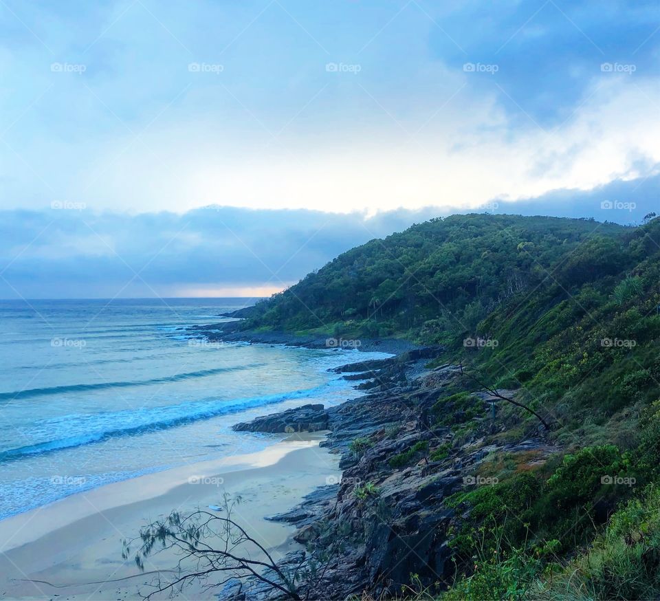 Early morning soft blue and purple light looking at the sea with a hill, cliffs and brush on a beach on the east coast of Australia 