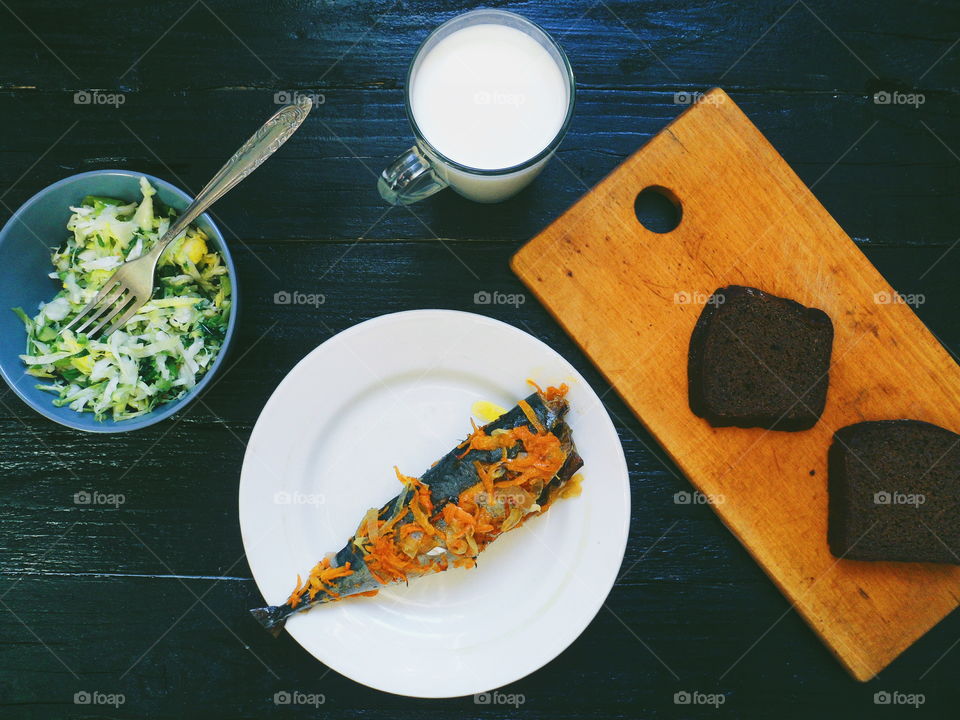 baked mackerel, vegetable salad, a cup of milk and bread on a black background, breakfast