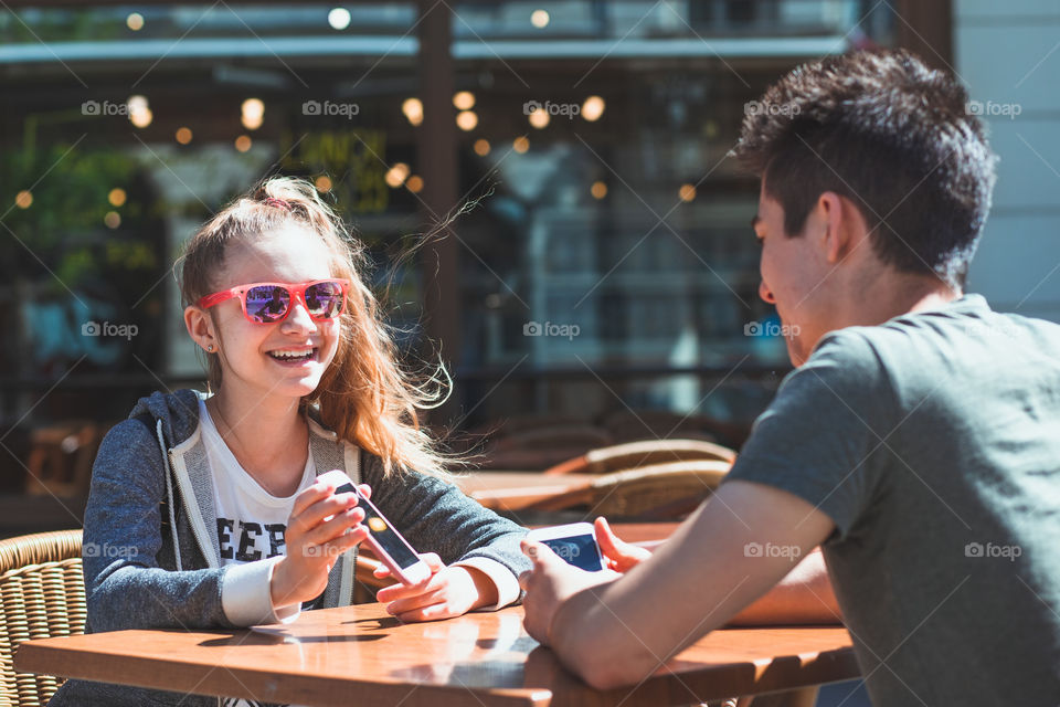 Young woman and man sitting in pavement cafe a the table talking and using mobile phones