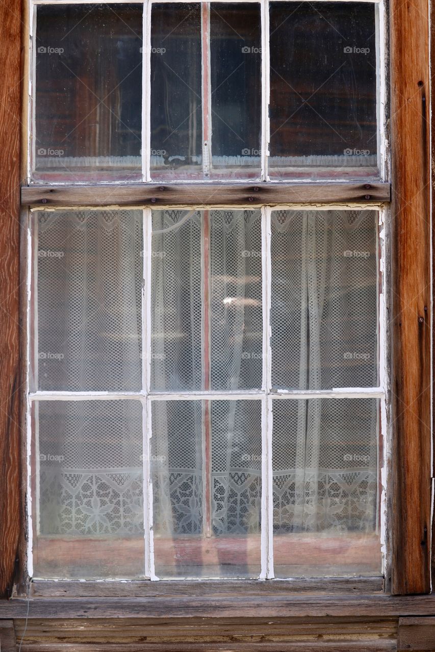 Eerie white pained window with lace curtains in abandoned old house 