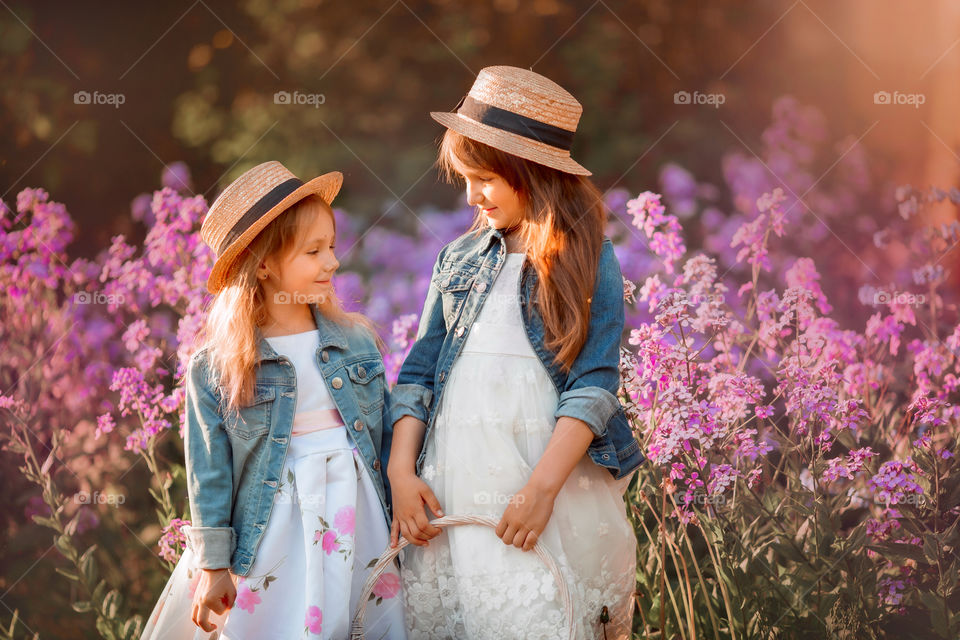 Little sisters in a blossom meadow at sunset 