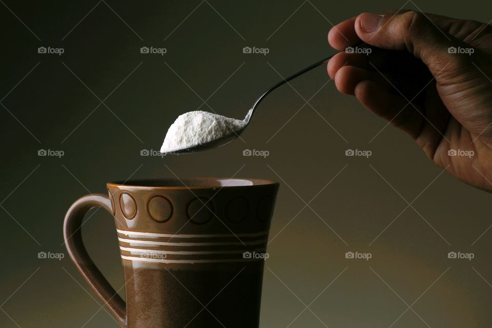 hand pouring coffee creamer on mug with a spoon