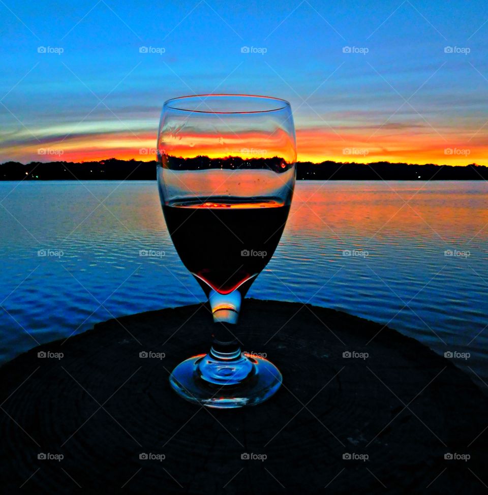 Blue x Orange - A glass of wine with the reflections of the orange sunset and the blue water and blue clouds 