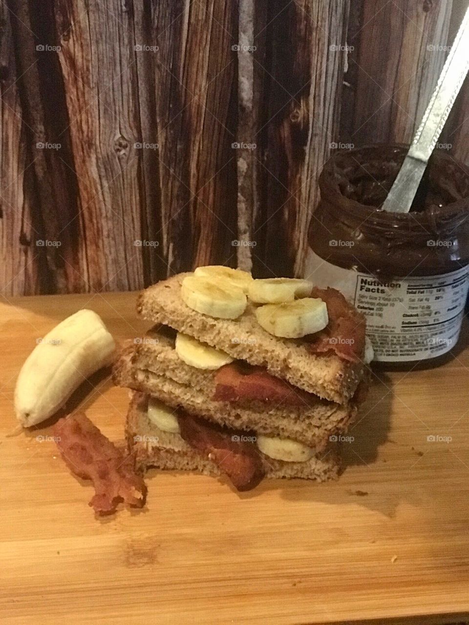 A Nutella, bacon and banana sandwich displayed on a cutting board against a wooden rustic background for lunch. USA, America