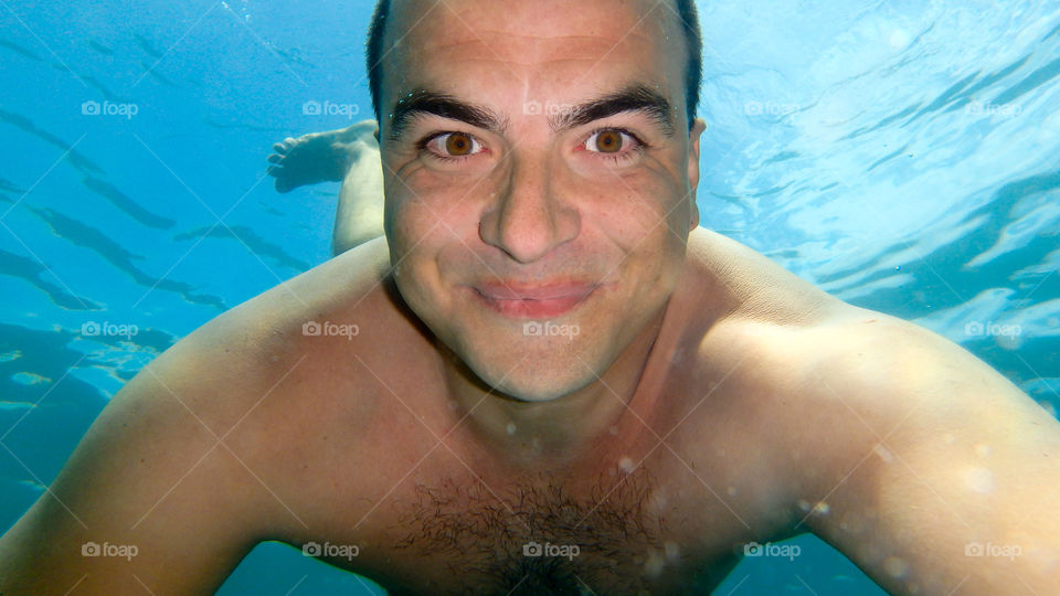 Man diving, male underwater smiling,swimming and relaxing in big blue sea with his camera