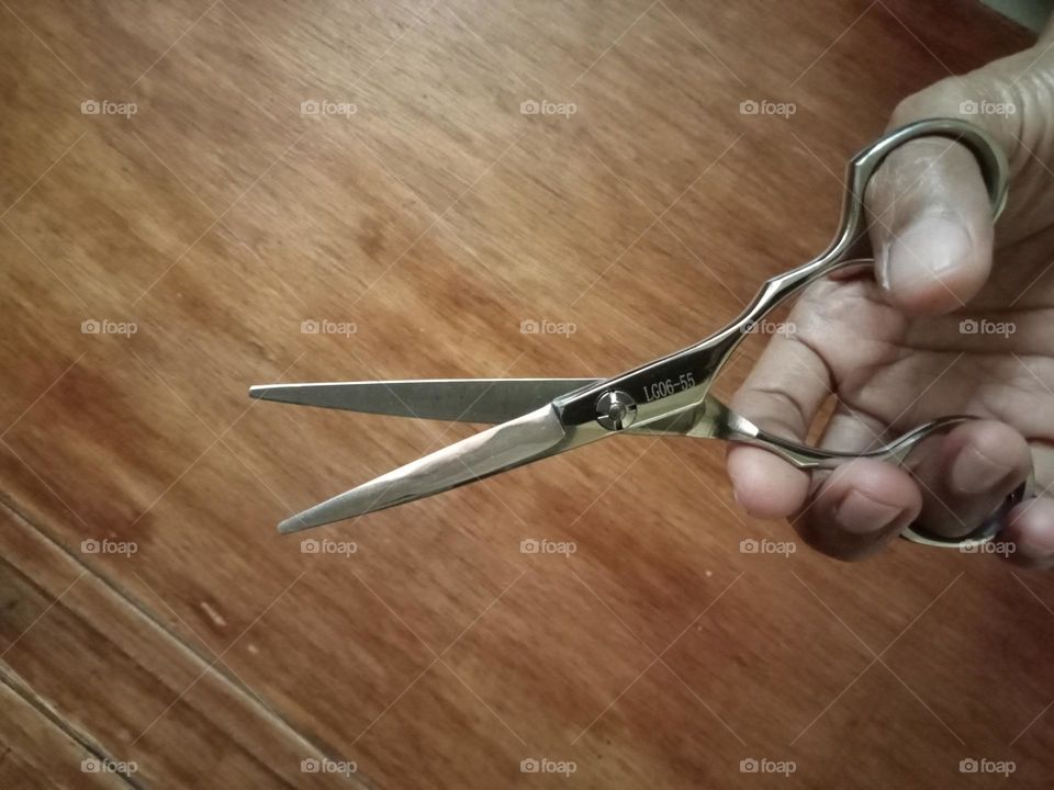 Hair scissors in a hand with wood board as background...