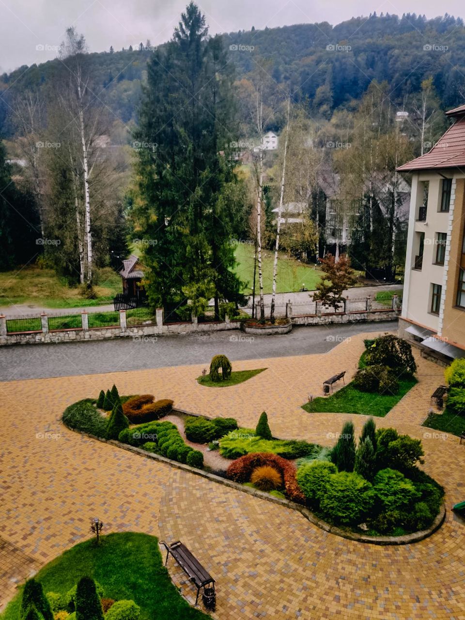 The hotel's inner yard with beautiful landscape design. Urban nature. Colorful plants are growing in the flowerbed. Bright colour bushes, greening of the territory. Multi storey building. Top view from the window. The hotel in the mountains