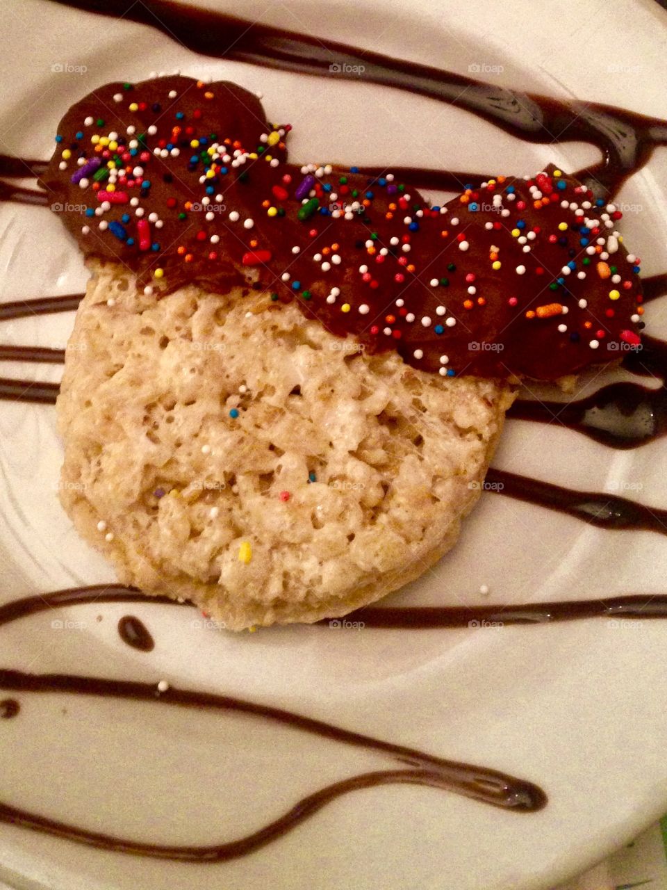 A homemade Rice Krispy Treat in the shape of Mickey Mouse and dipped in chocolate with rainbow sprinkles 