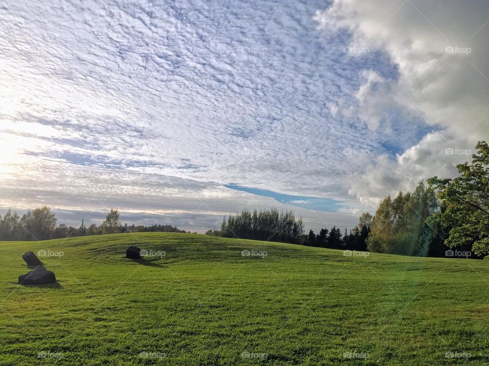 Beautiful tranquil landscape over green hill meadow with few stones under the cloudy sky with low sun light 