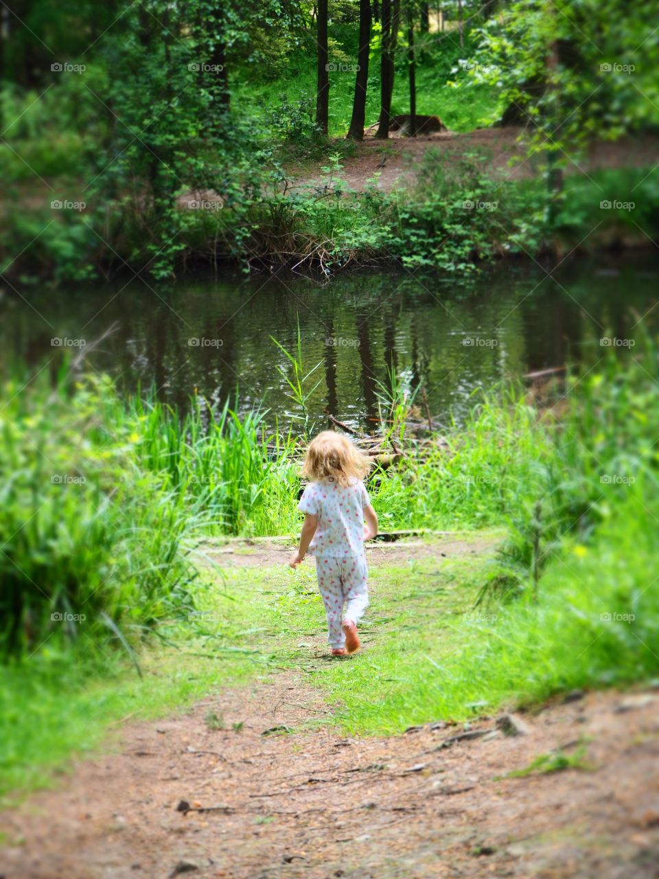 Child running down path to pond under tree canopy