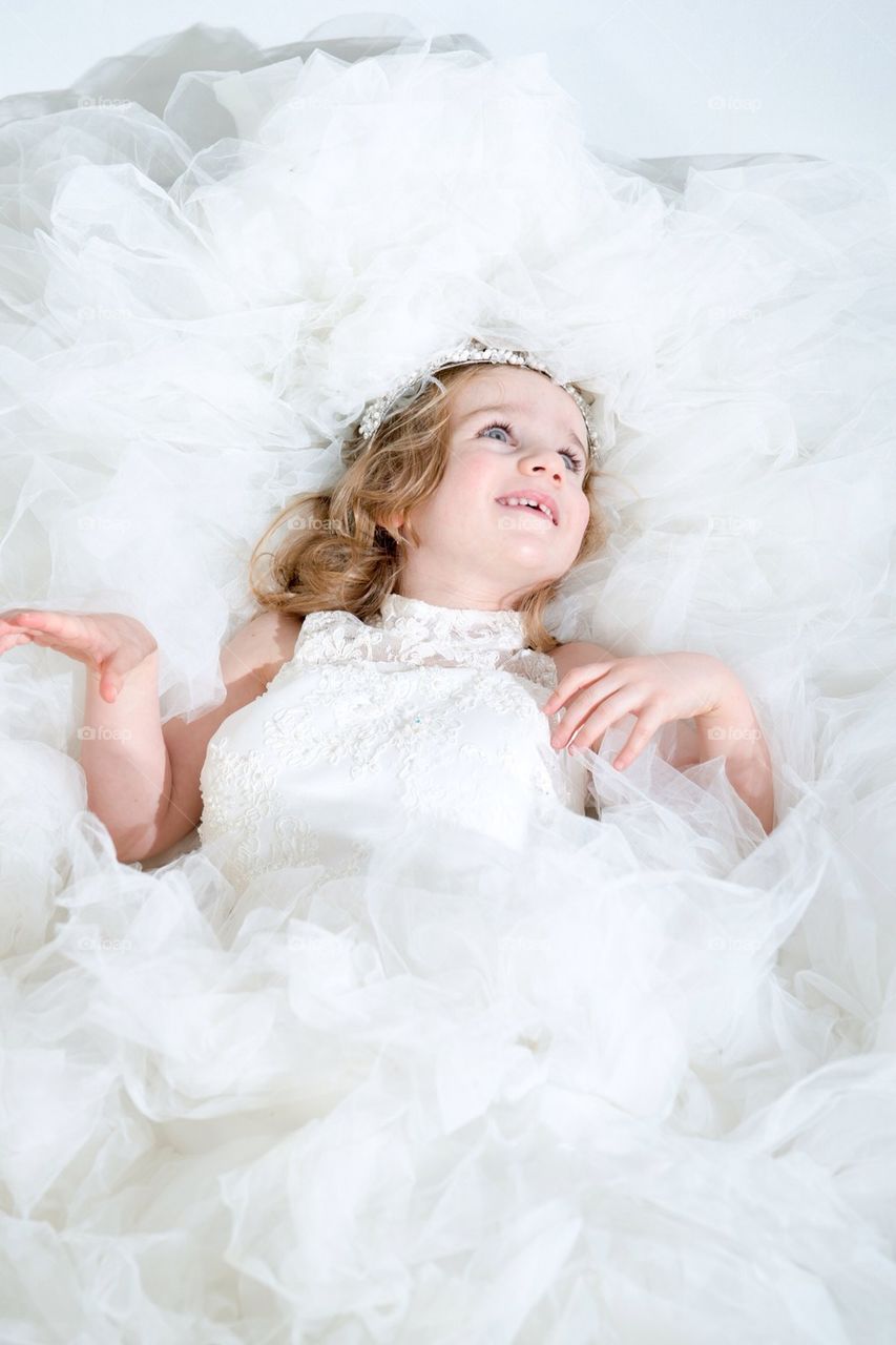 A Beautiful girl (child) in an adult wedding dress with tiara smiling while looking away from the camera. 