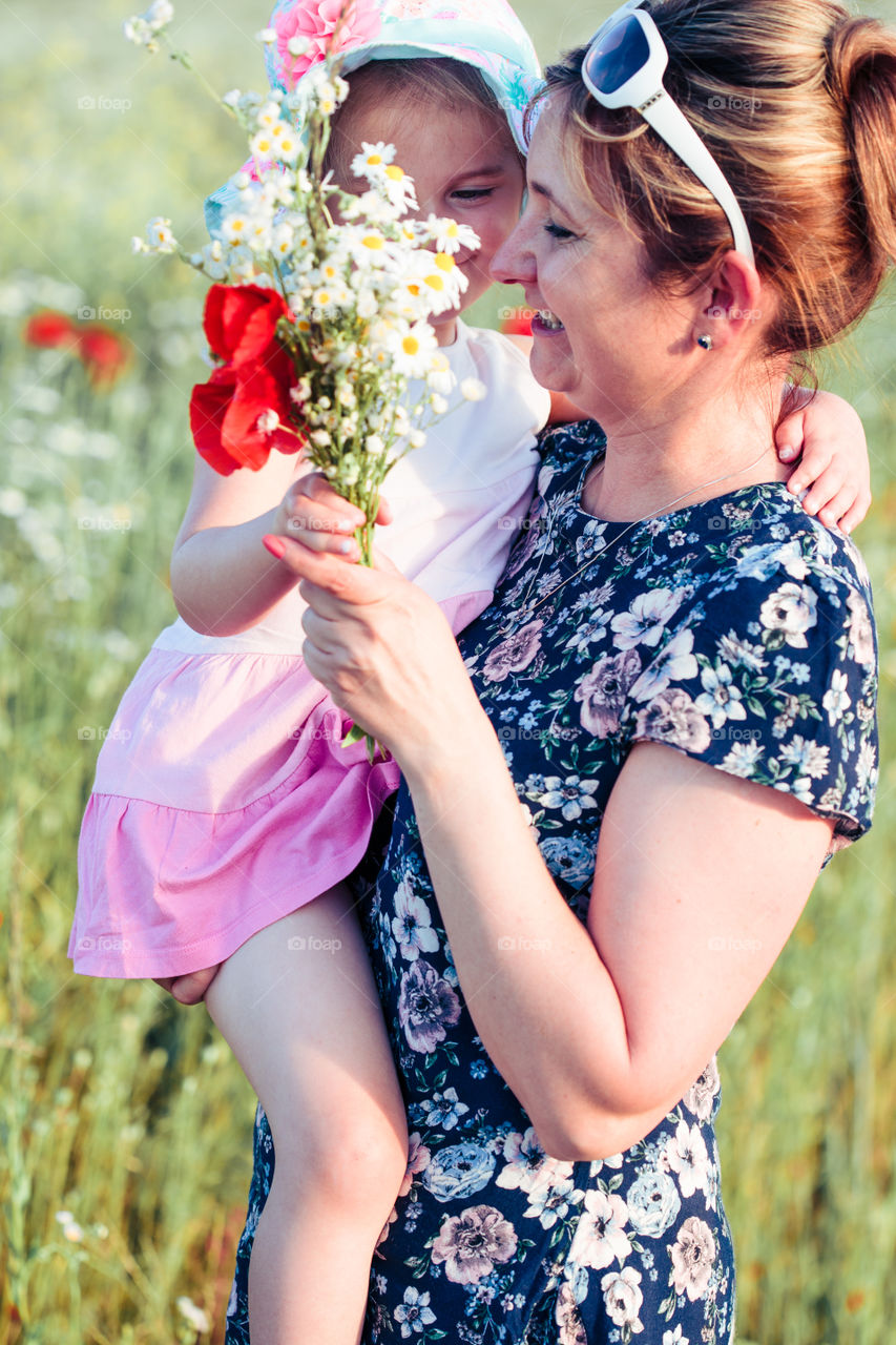 Mother and her little daughter in the field of wild flowers. Little girl picking the spring flowers for her mom for Mother's Day in the meadow. Nature scene, family time