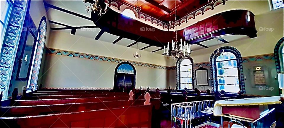 Inside the synagogue in Bavaria, Germany is a duplex cathedral ceiling, an upstairs section w beautiful polished cherry or mahogany wood railings, rounded edges, lovely detail in the lower section ceiling with wood inlays. 2021. Hypnotic Productions