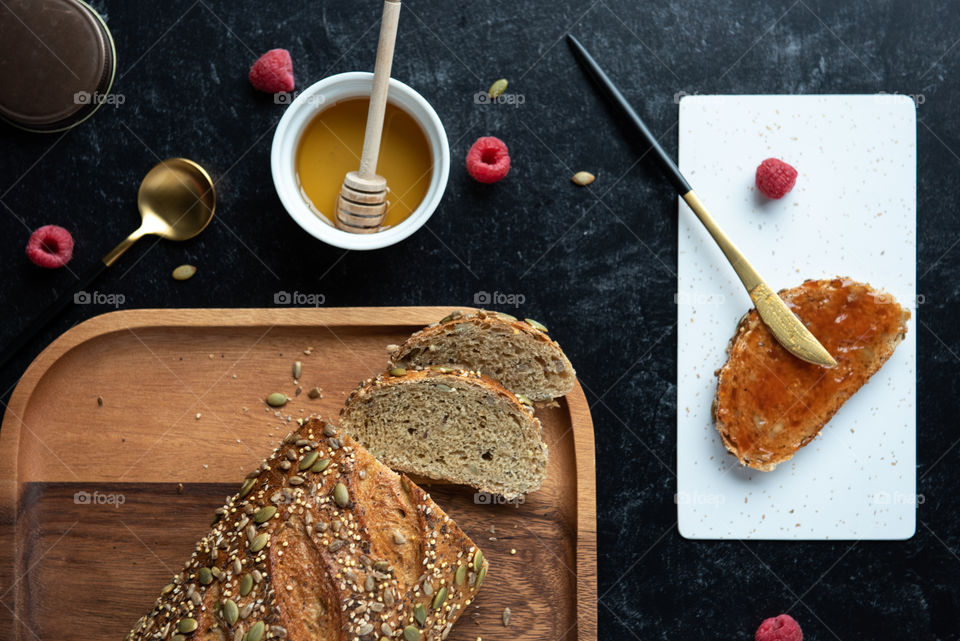 Flat lay of a loaf of bread on a wooden plate with a slice of toast and honey and jelly