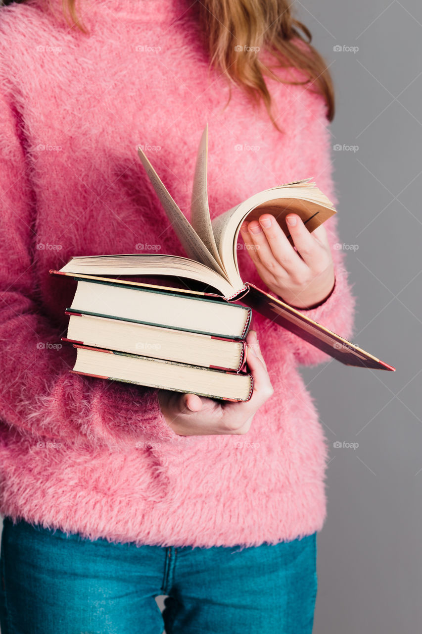 Young girl holding a few books. Teenager girl wearing pink sweater and blue jeans. Vertical photo