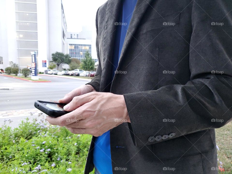 Closeup of a man wearing a brown corduroy blazer. He is on his cell phone just outside of a business center.