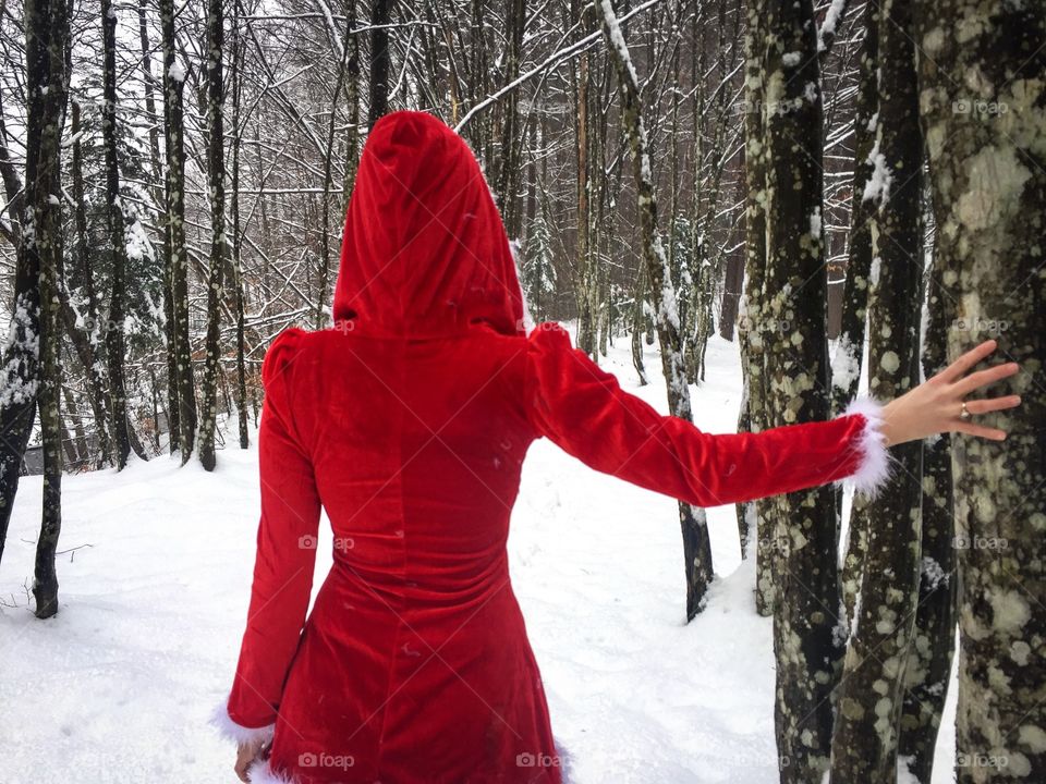 Back of woman wearing red coat with red hood in a forest of snowy trees
