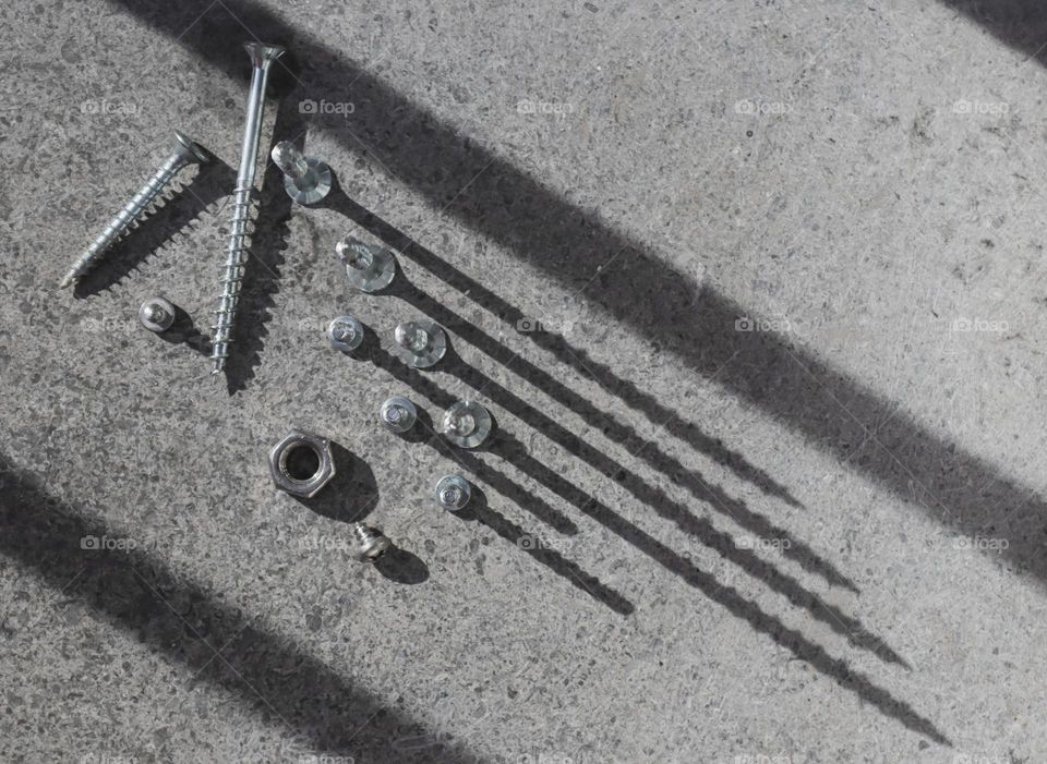 Screws and bolts lie on a stone background with geometric long soft tenchmi from the sun, flat lay close-up. The concept of tools,metal, construction, repair.