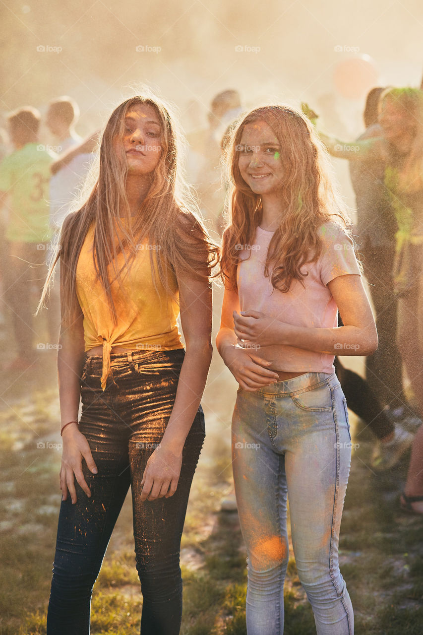 Portrait of happy smiling young girls with colorful paints on faces and clothes. Two friends spending time on holi color festival