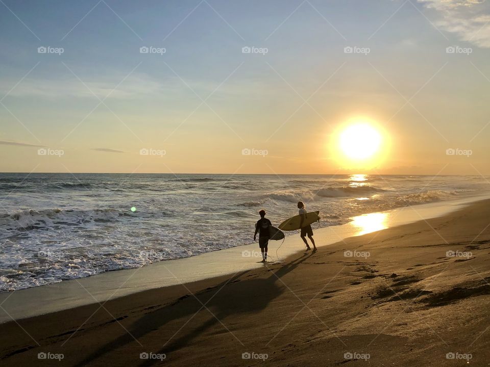 Two surfers run along the quiet beach to get to the water for a sunset surf session