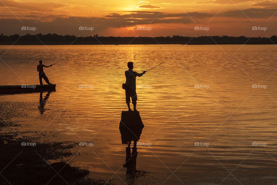 Silhouette of fisherman fishing in sea during sunset