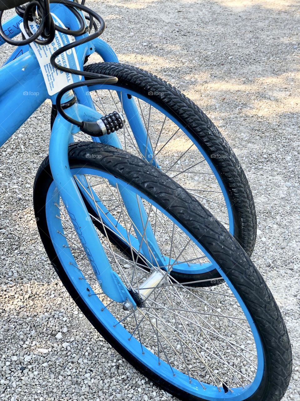 Closeup of front tires of parked blue rental bikes. A combination lock hangs from the handlebars 